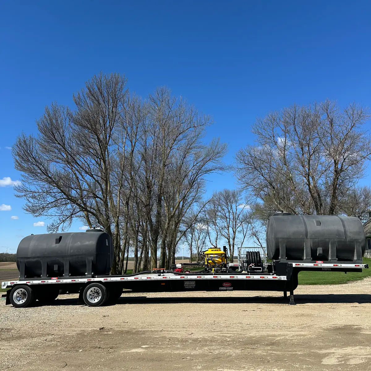 Full-length custom nurse trailer with dual black poly tanks on a flatbed semi, built by Dahl Farm Supply